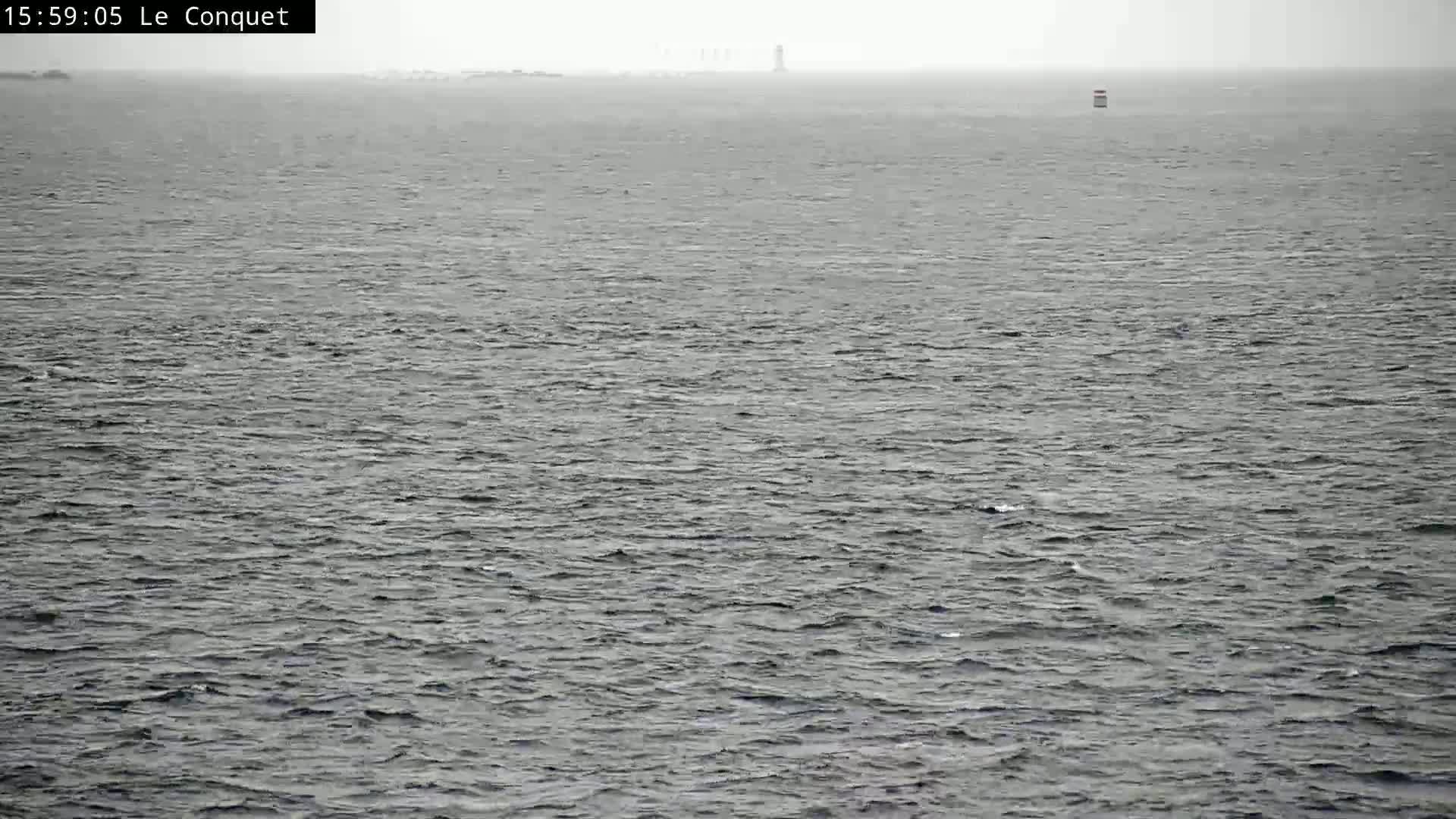 A hazy, overcast day shows a vast expanse of choppy gray water with a distant lighthouse and a small marker buoy visible on the horizon.