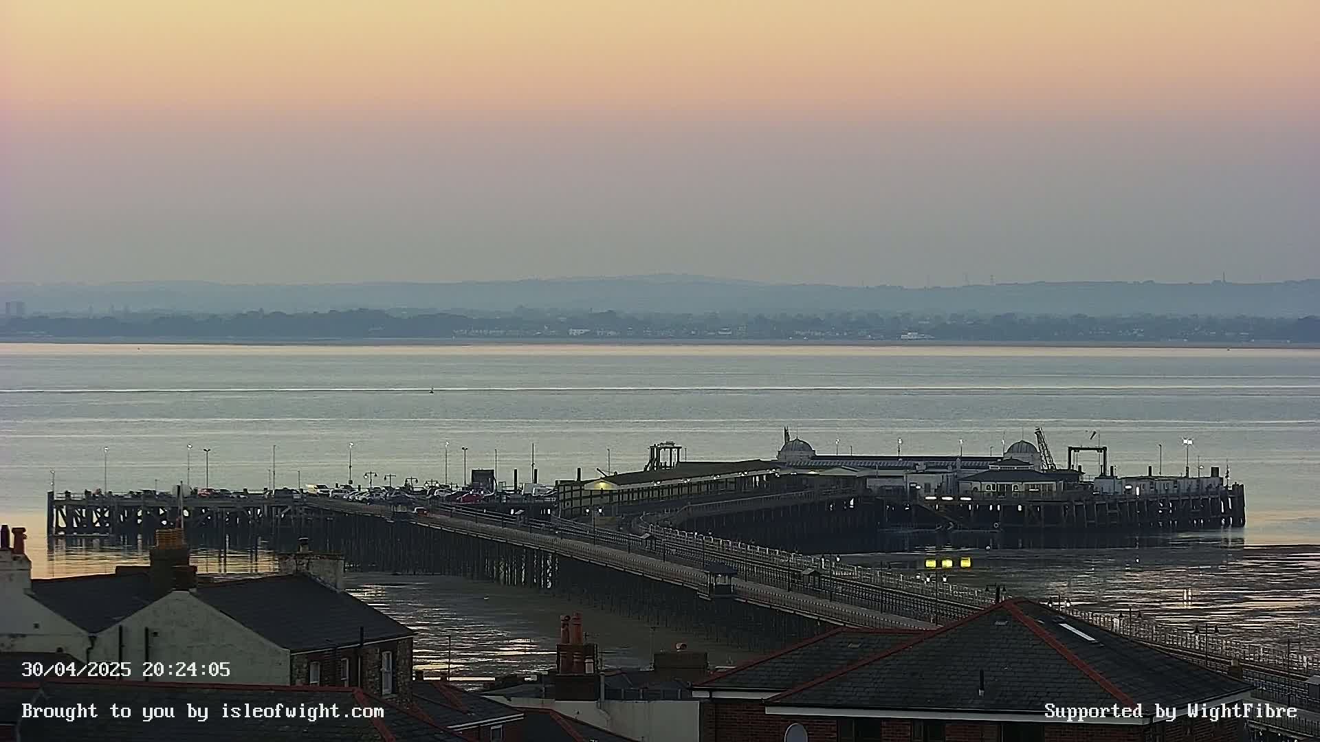 A long pier extends into a calm body of water under a pale, dusky sky.