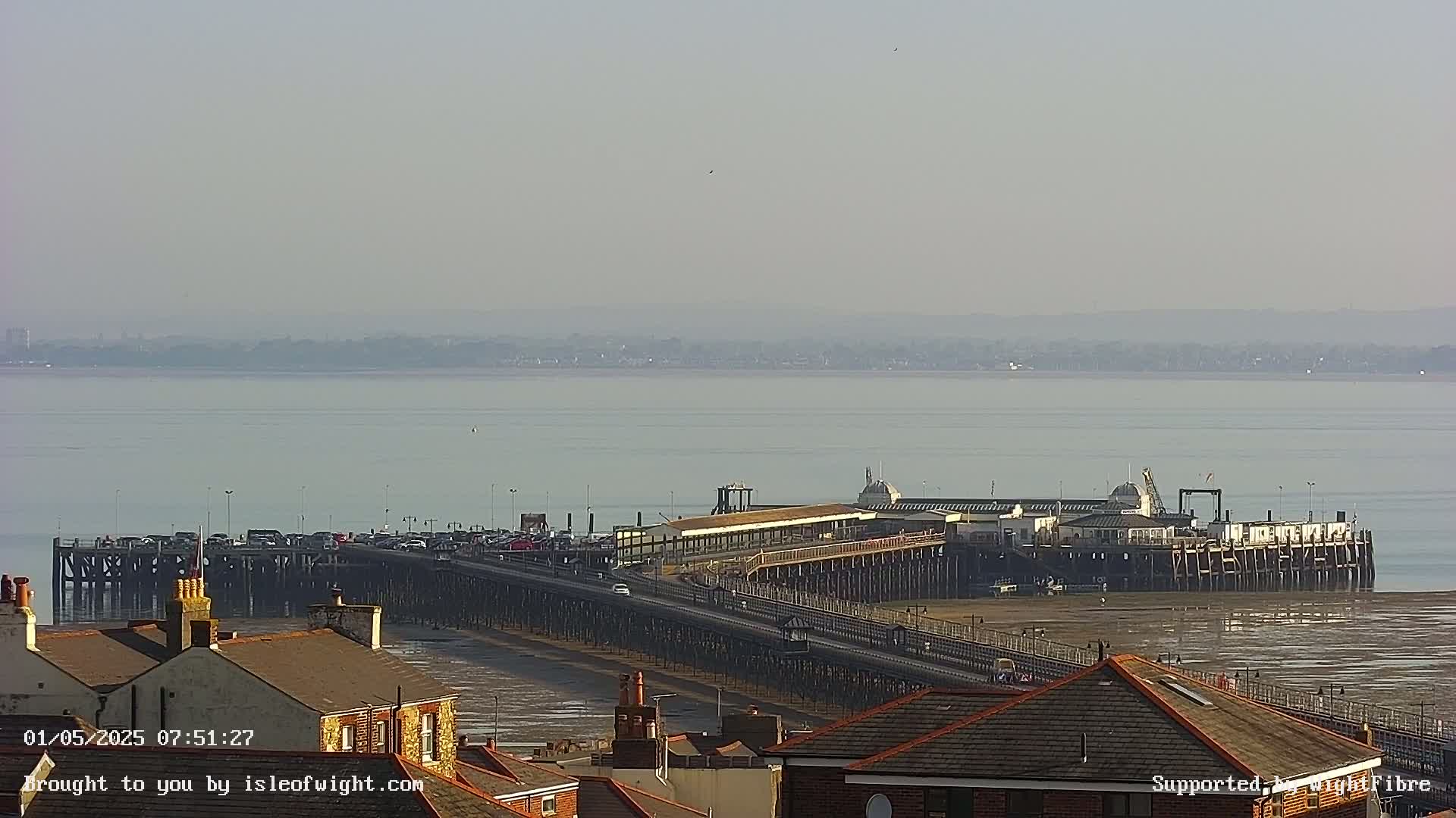 A long pier extends into a calm, hazy body of water, with buildings and rooftops visible in the foreground.