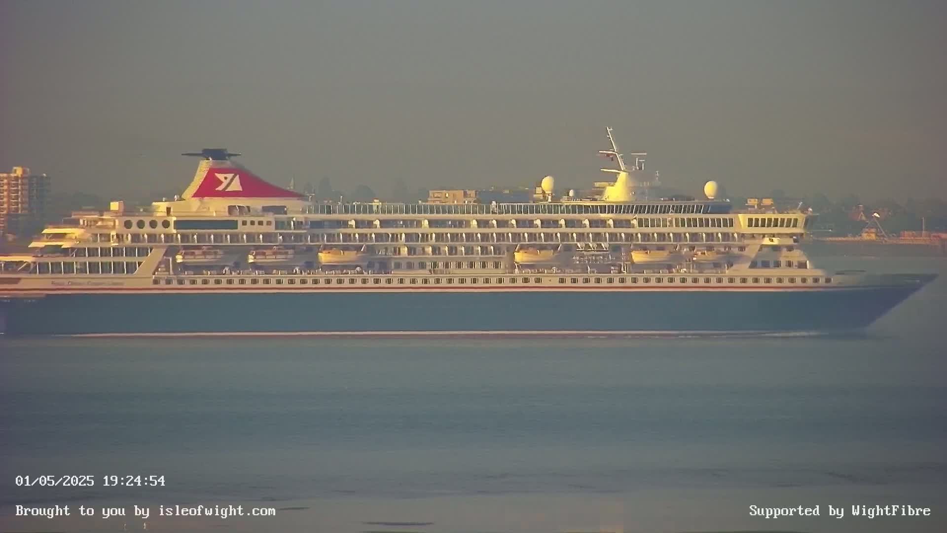 A large cruise ship sails on calm water under a hazy, muted-light sky.