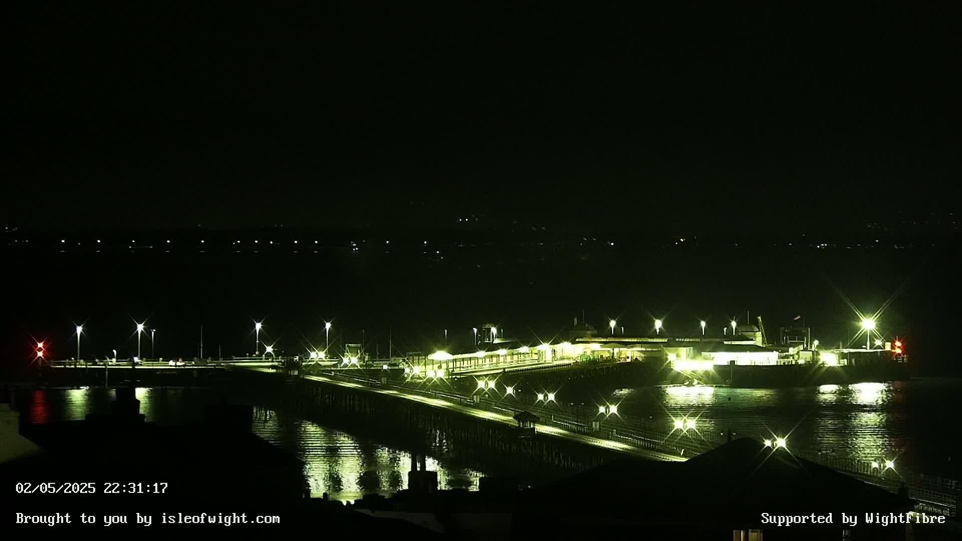 A brightly lit pier extends over dark water at night.
