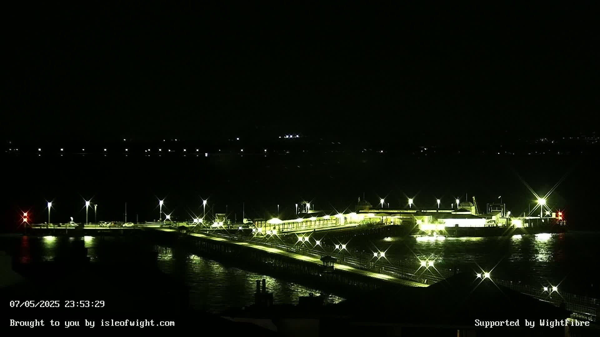 A brightly lit pier extends over dark water at night.
