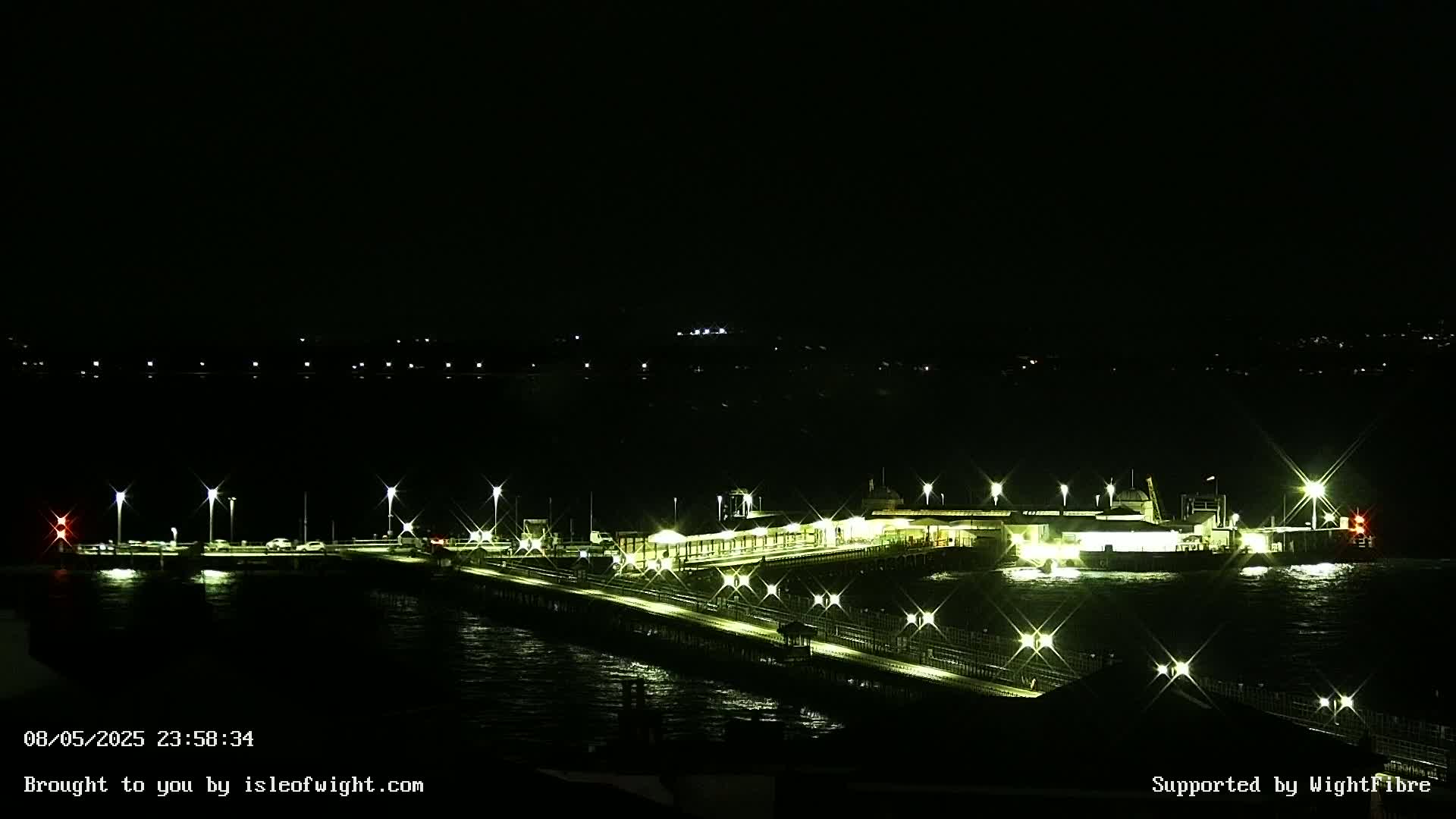 A brightly lit pier and ferry terminal are visible at night, with choppy water surrounding them.