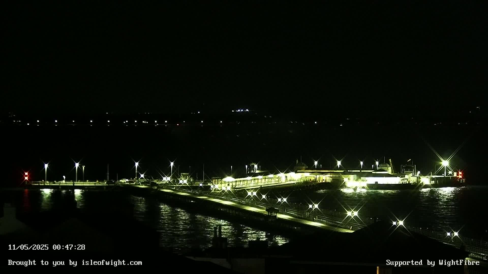 A brightly lit pier extends into dark, choppy water at night.