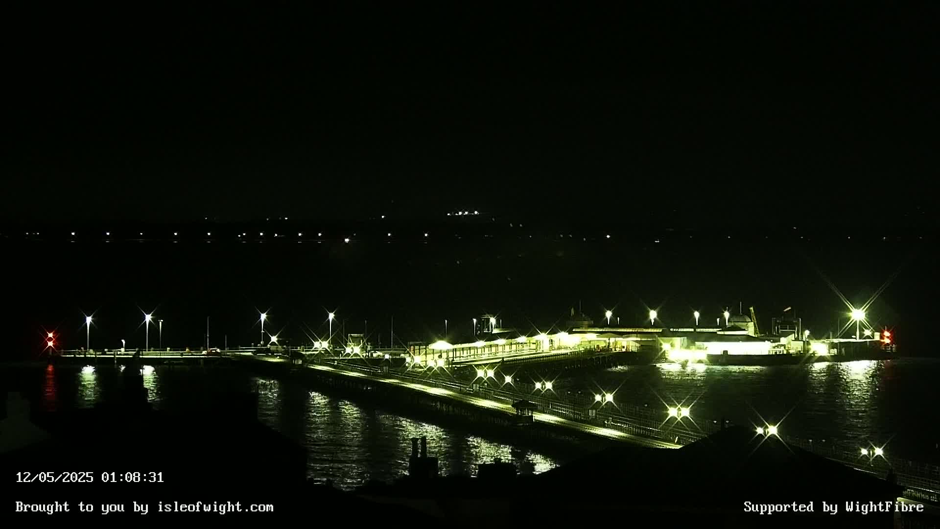 A brightly lit pier and ferry terminal extend into dark, nighttime water.