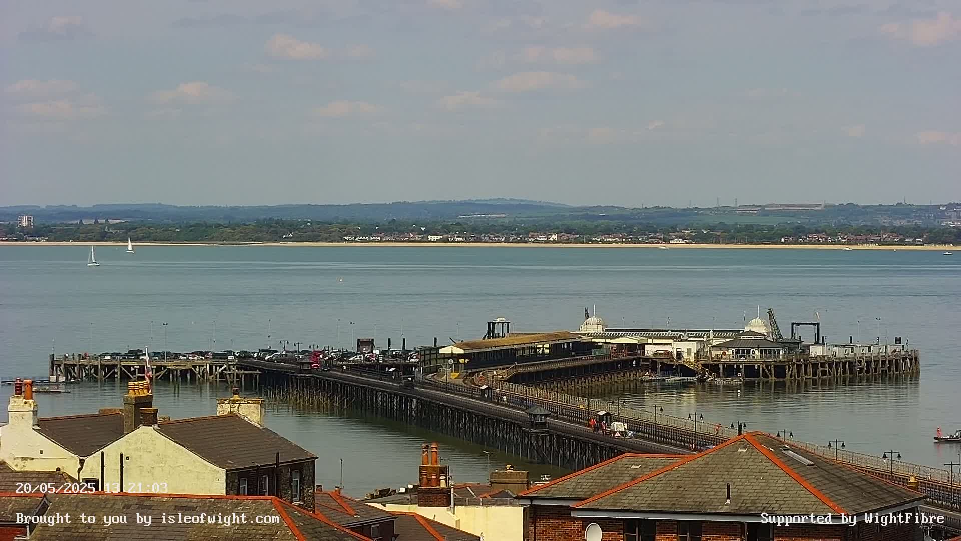 A long pier extends over calm water toward a distant shoreline under a partly cloudy sky.