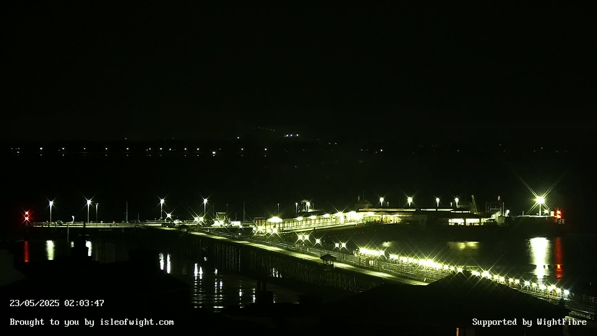A brightly lit pier extends over dark water at night.
