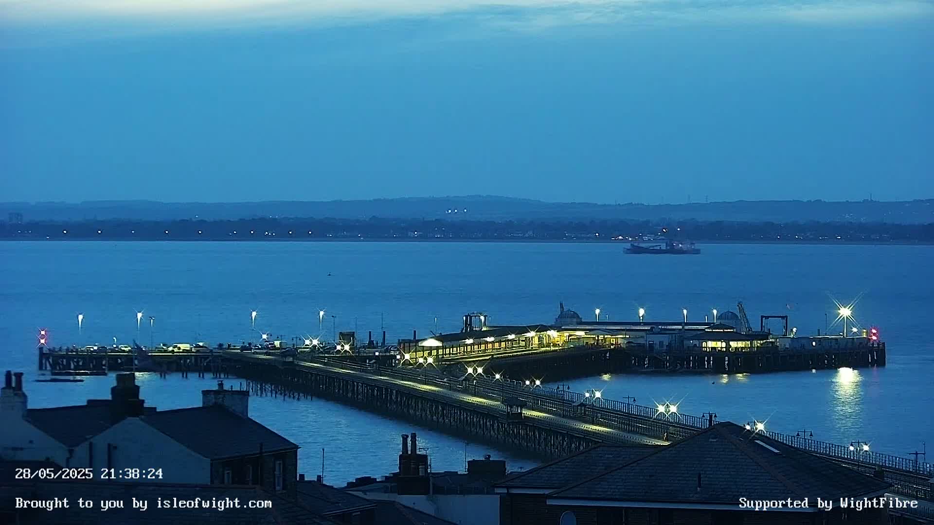 A long pier with lights illuminating the pathway and building, extending into a dark-blue body of water under a twilight sky.