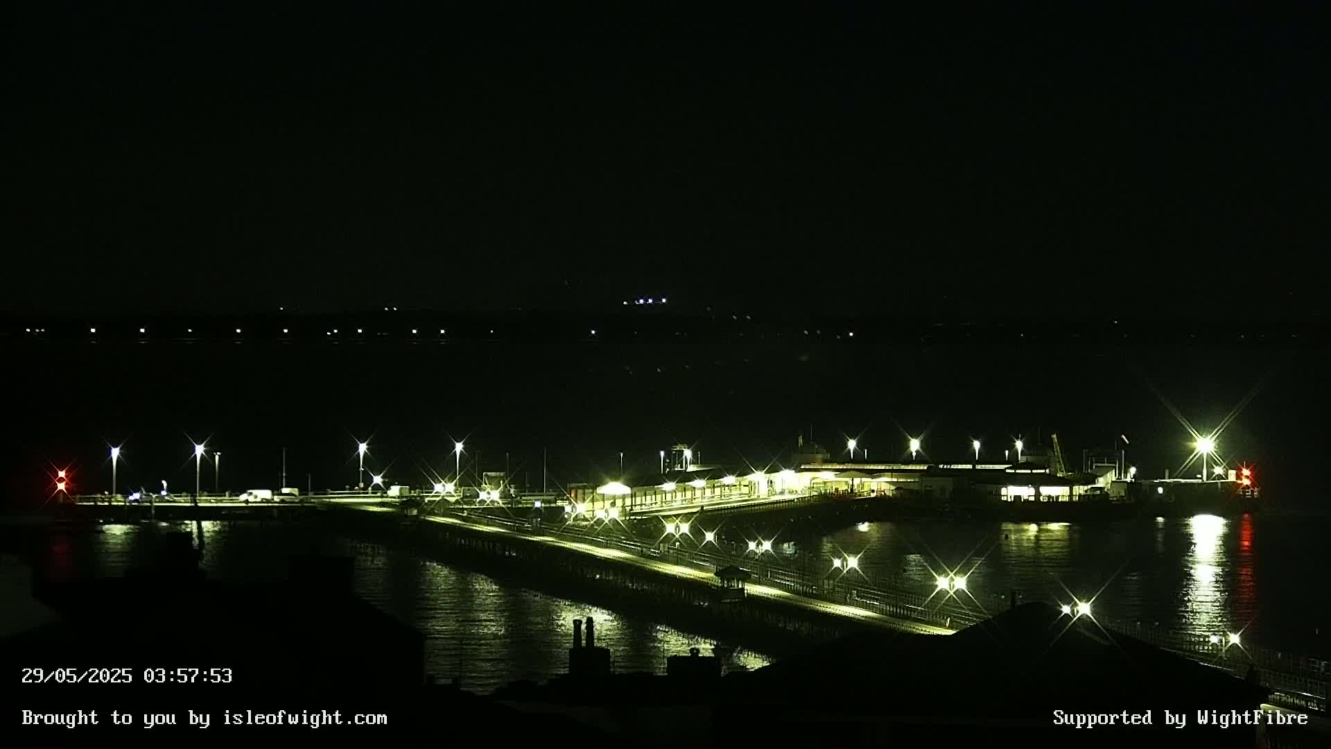 A brightly lit pier extends over dark water at night.