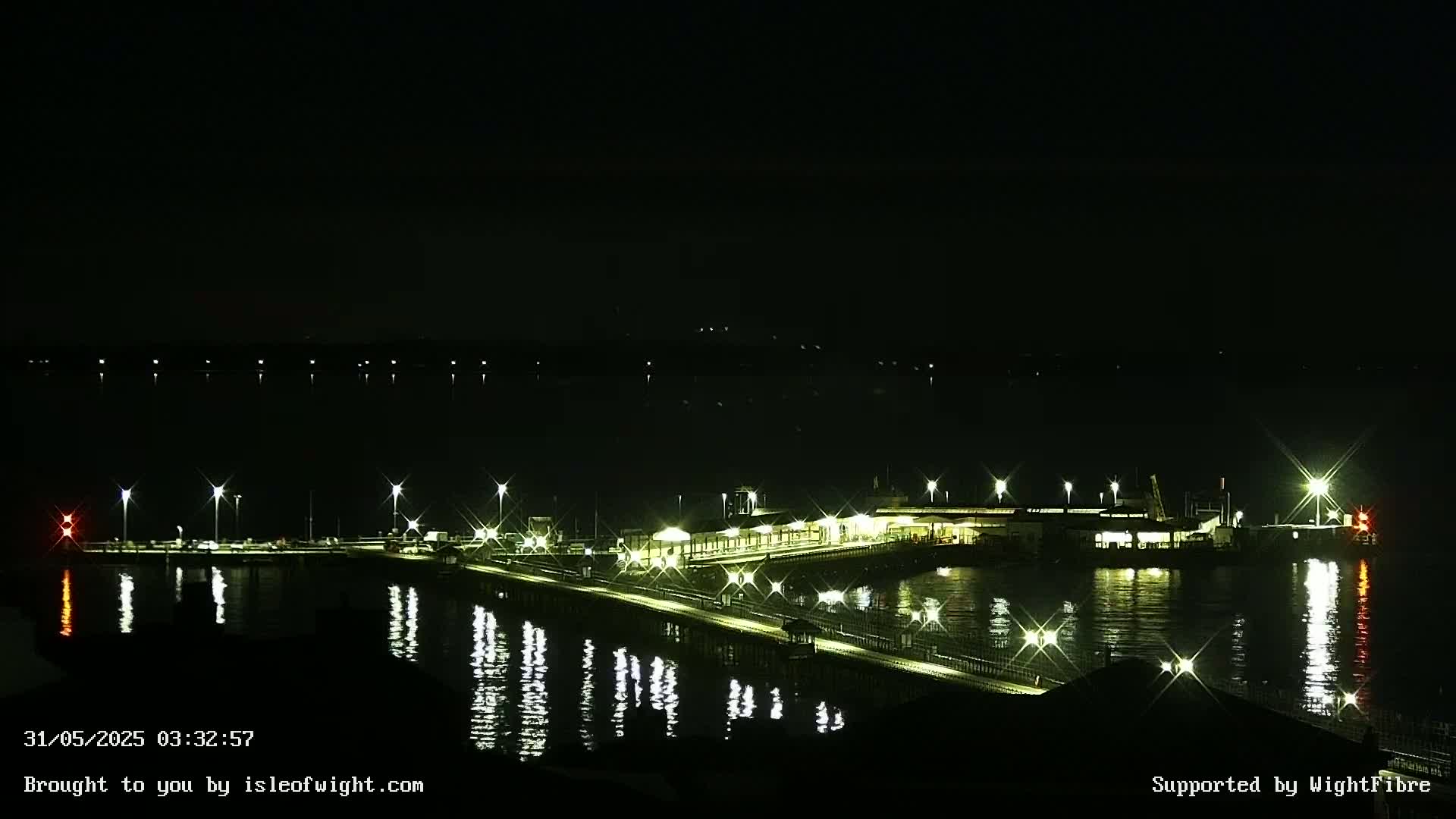 A brightly lit pier extends into a dark, calm body of water at night.