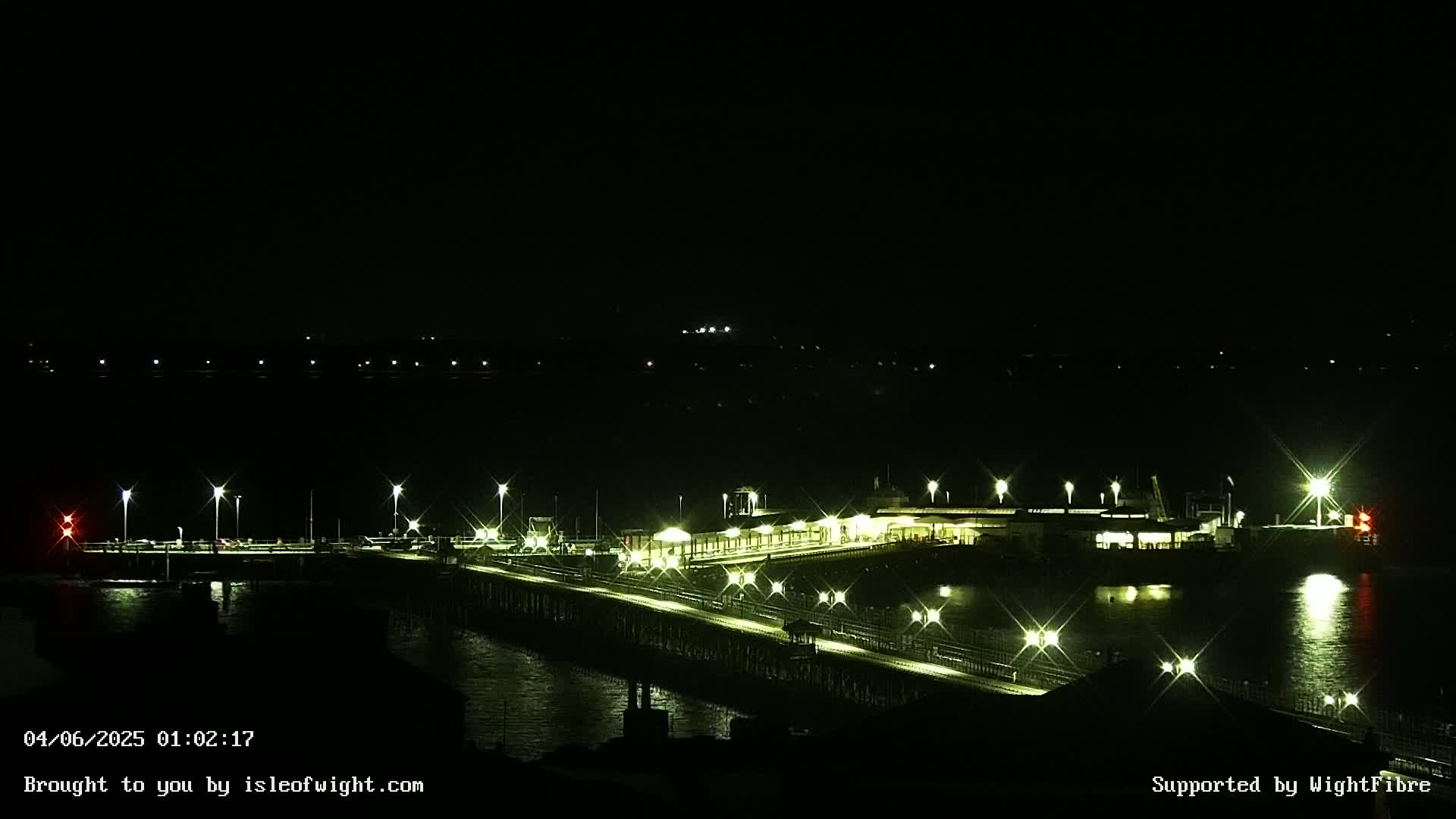 A long, brightly lit pier extends over dark water at night.