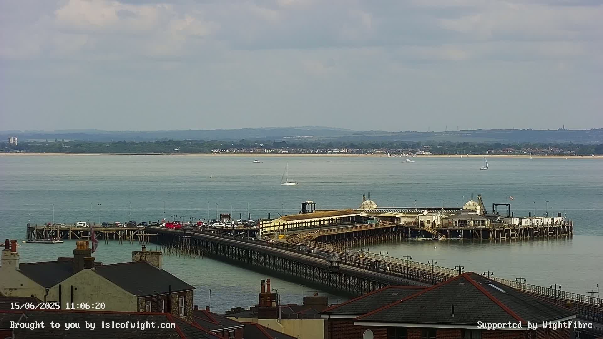 A long pier extends into calm, grey-green water under a partly cloudy sky, with a distant shoreline visible in the background.