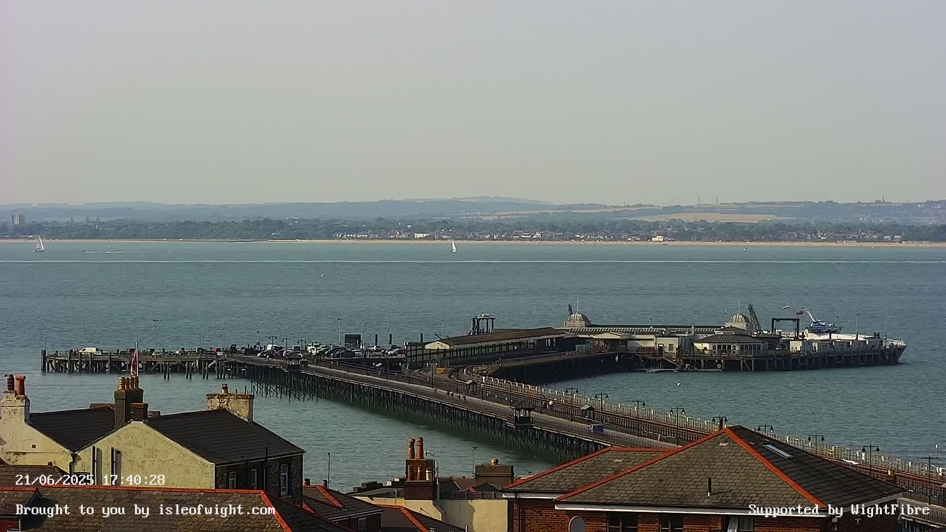 A long pier extends into a calm body of water on a hazy day, with a distant shoreline visible.