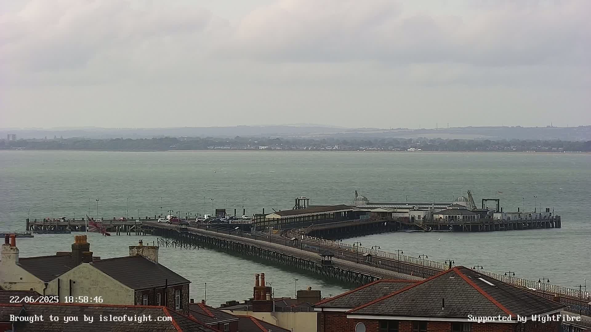 A long pier extends into a calm, gray body of water under an overcast sky.