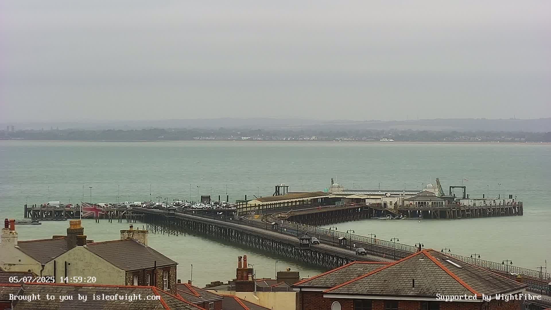 A long pier extends from a shoreline into a calm, grey sea under an overcast sky.