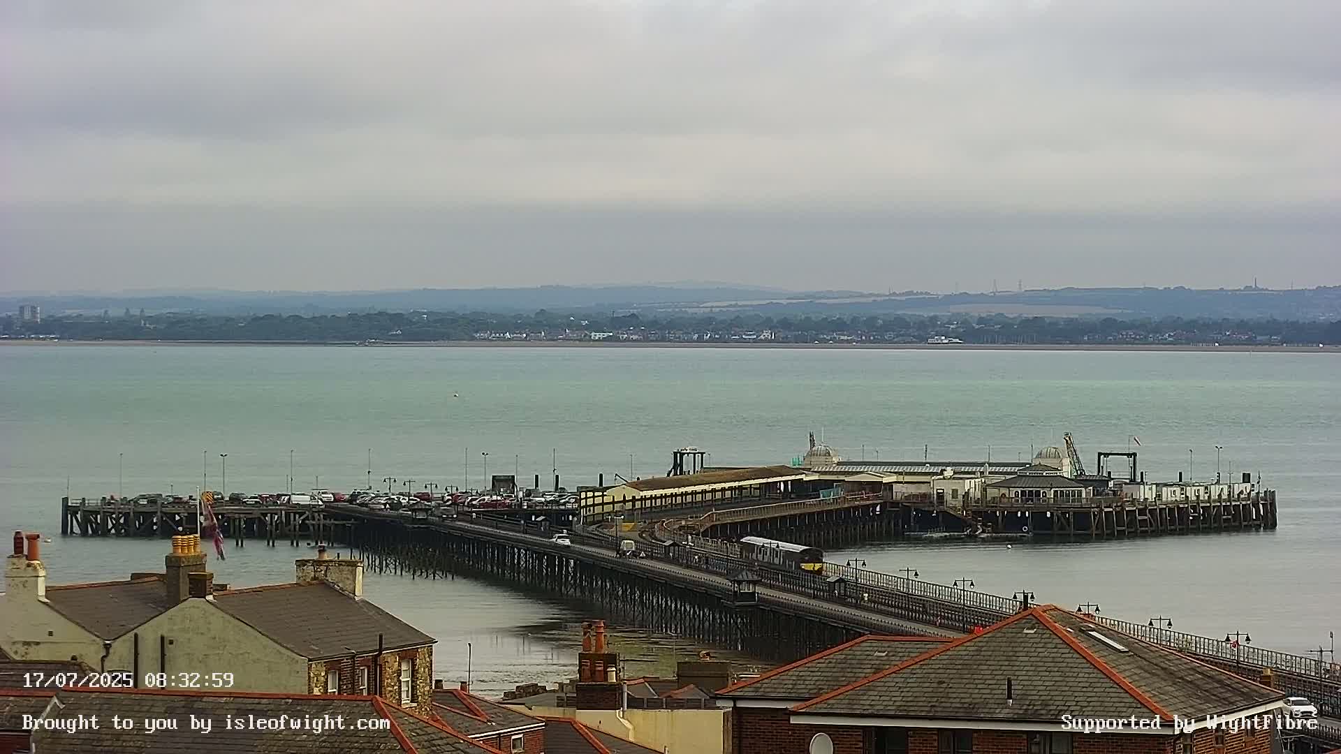 A long pier extends into a calm, light-green body of water under an overcast sky.