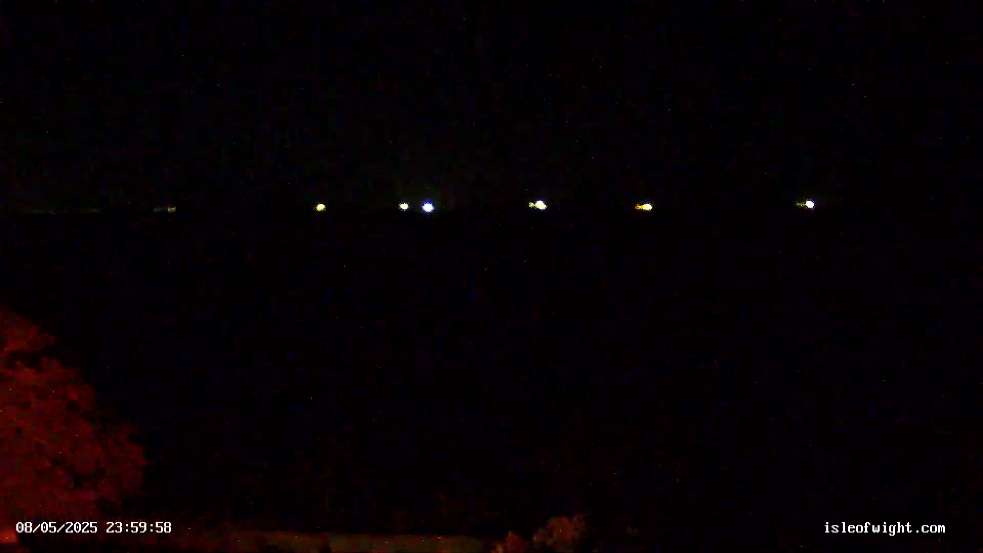 A dark nighttime scene shows a line of distant lights across a black horizon.