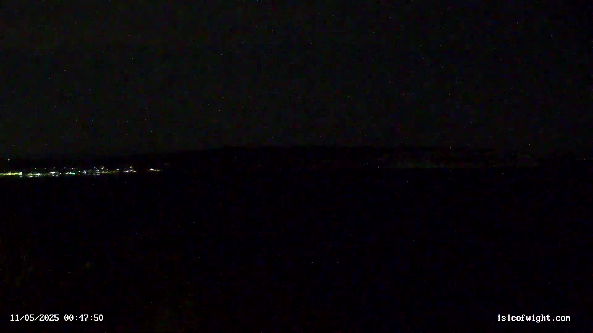 A dark, nighttime scene shows a distant line of faint lights, possibly a town, under a starlit sky.