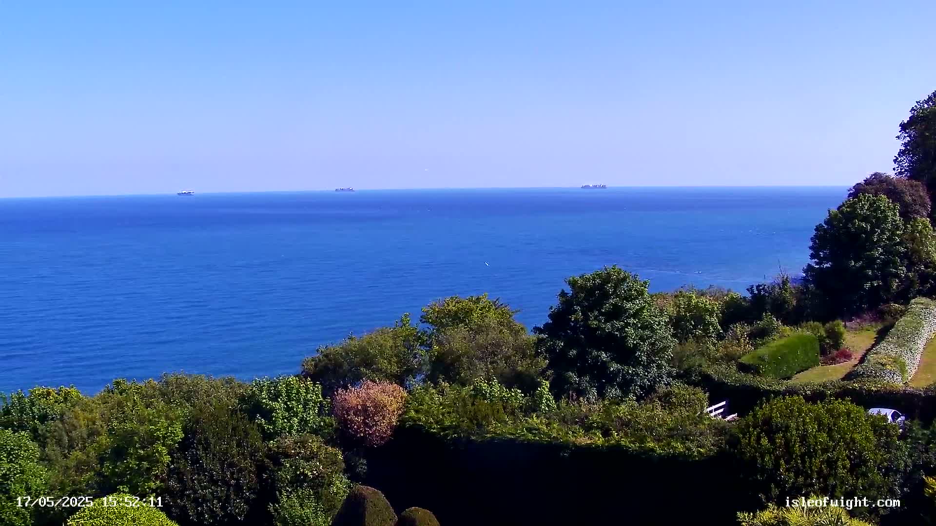 A tranquil ocean view on a clear day, seen from a garden overlooking a coastline with lush green foliage.