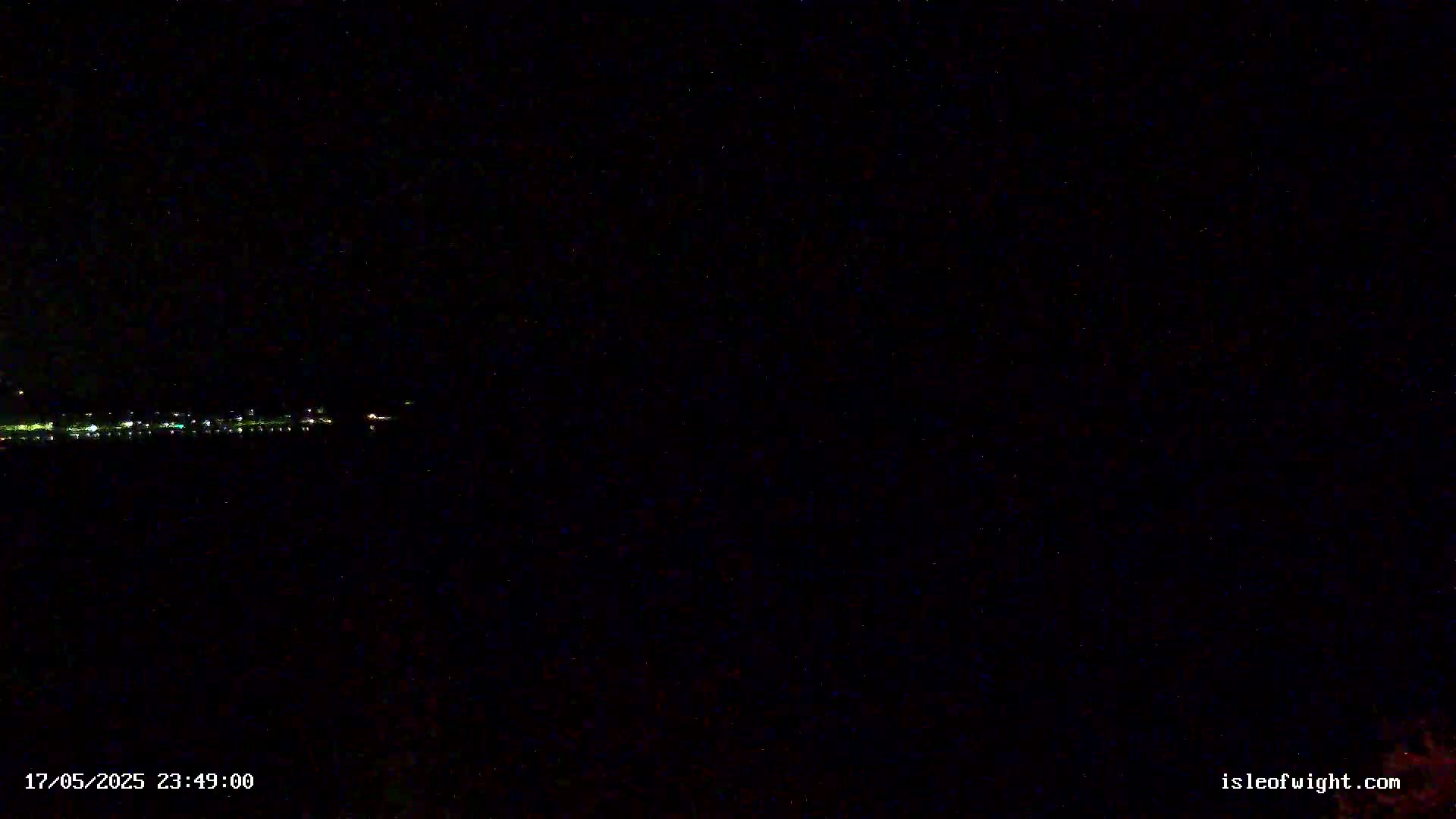 A dark, nighttime scene shows a distant line of faint lights across a body of water under a clear, starry sky.