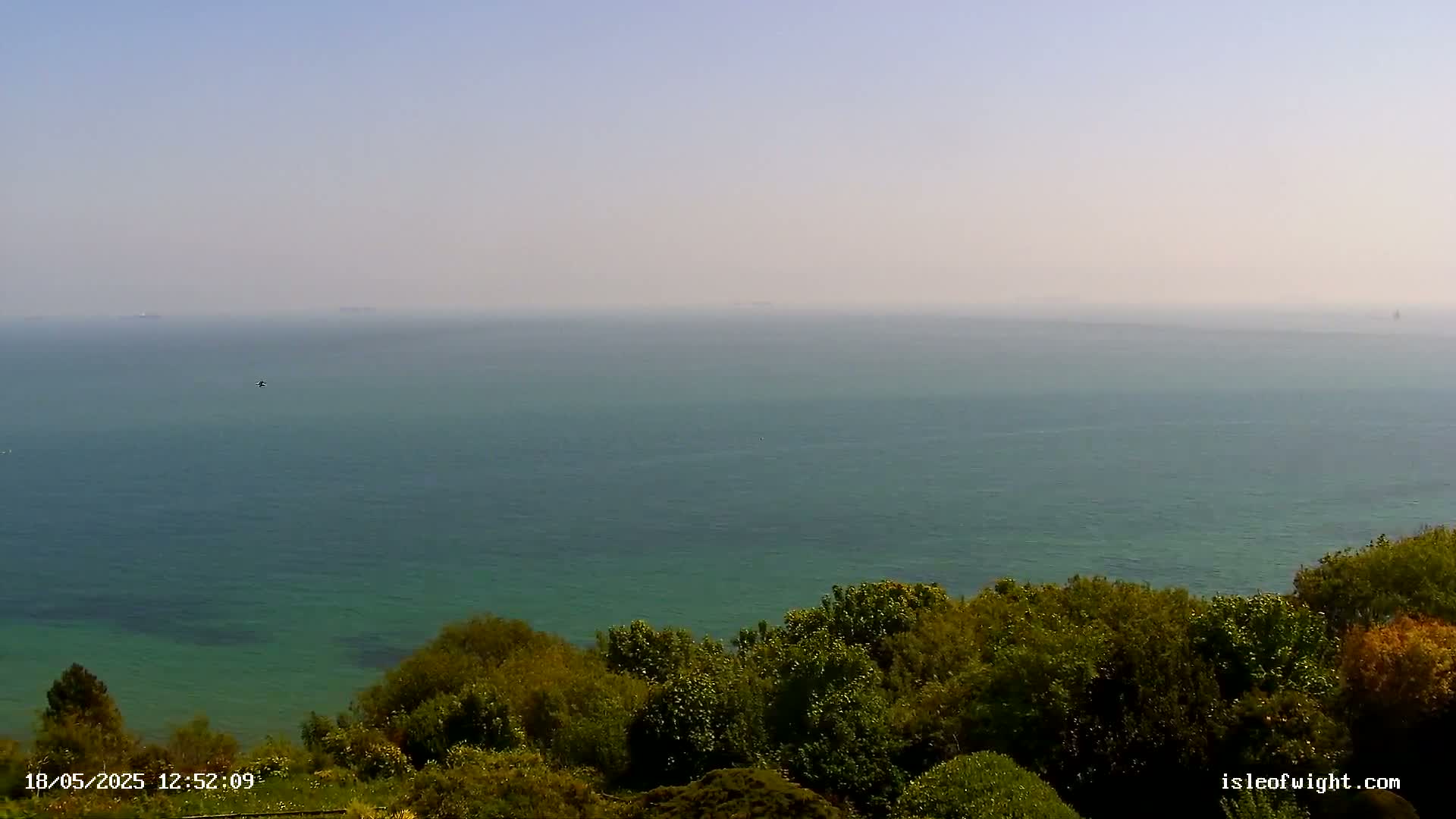 A hazy, sunny day reveals a vast expanse of teal ocean meeting a lush, green clifftop.