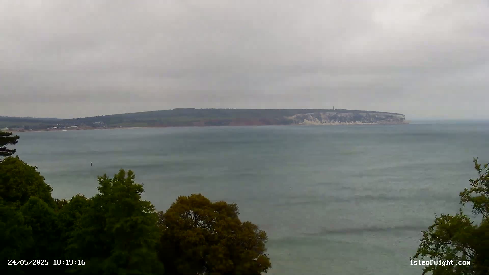 A body of water with small waves stretches to a distant landmass under an overcast sky.