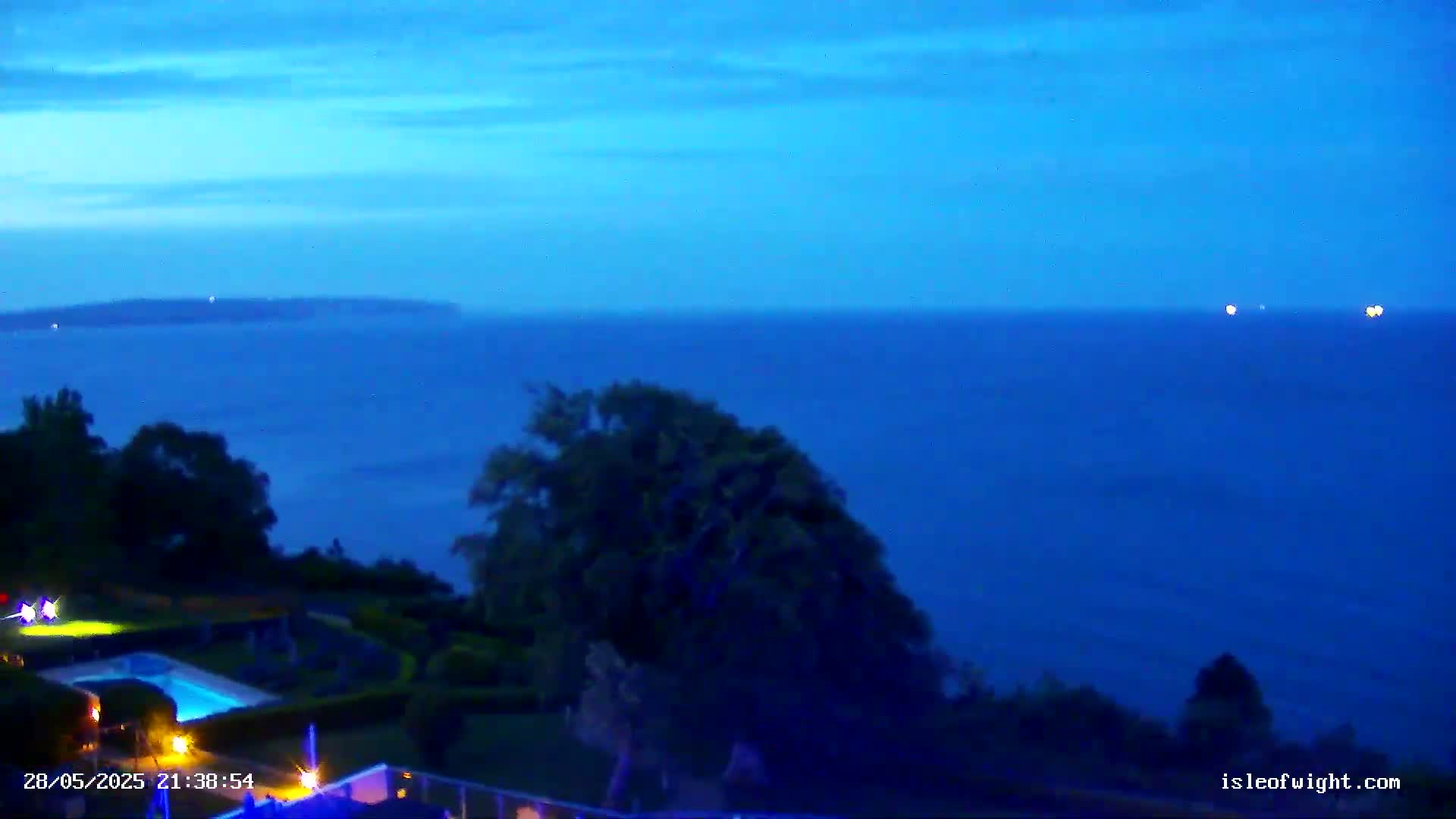 A nighttime view shows a dark blue sea under a twilight sky, with a swimming pool and vegetation visible in the foreground.
