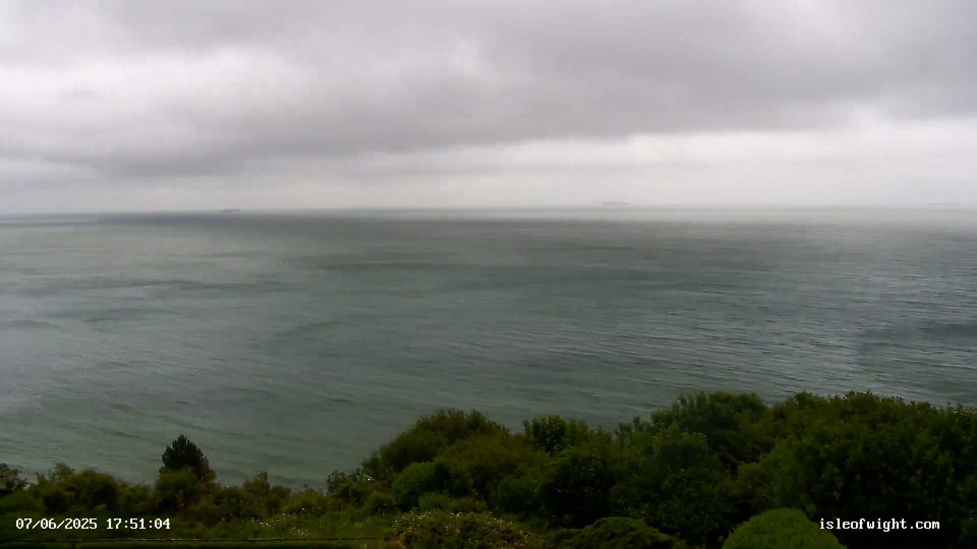 A large body of dark-green water stretches to a hazy horizon under a cloudy, overcast sky.