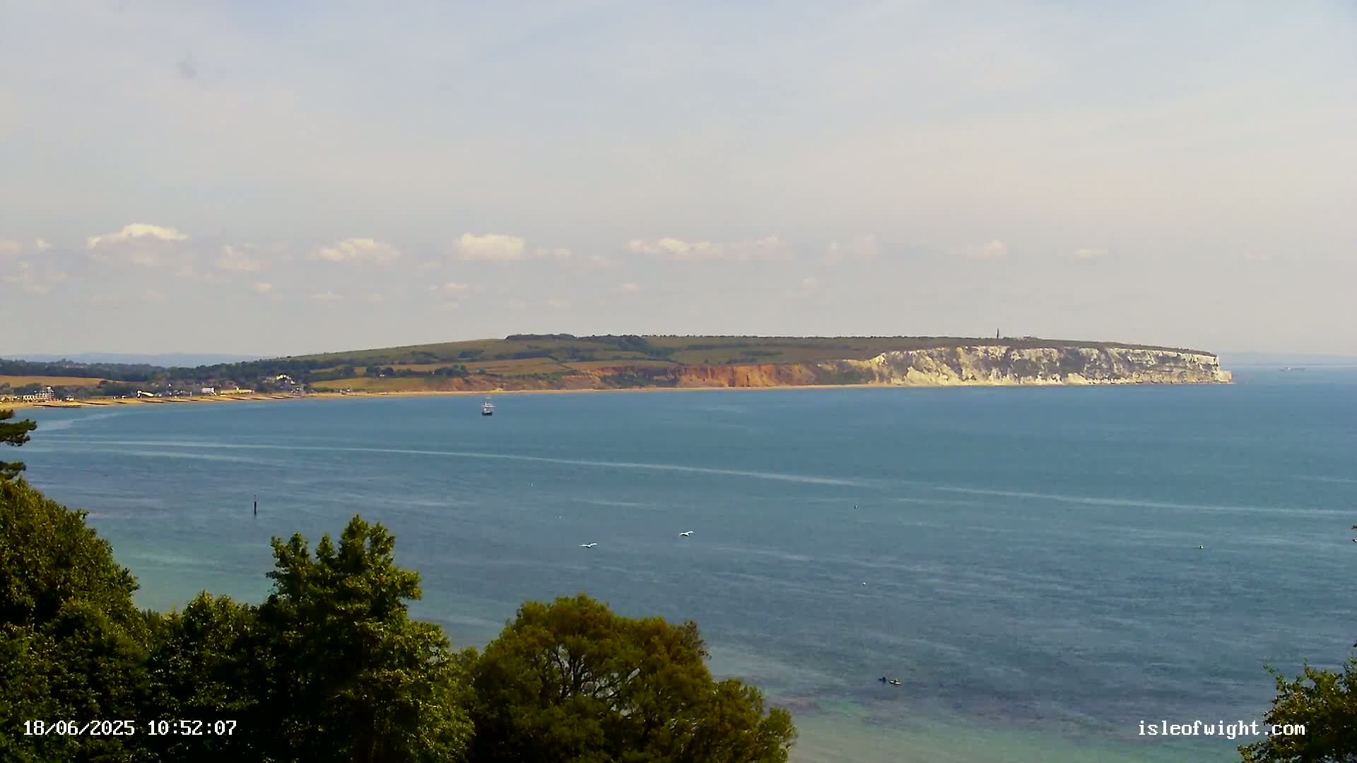 A body of water stretches out to a distant coastline featuring a long stretch of cliffs and green hills under a partly cloudy sky.