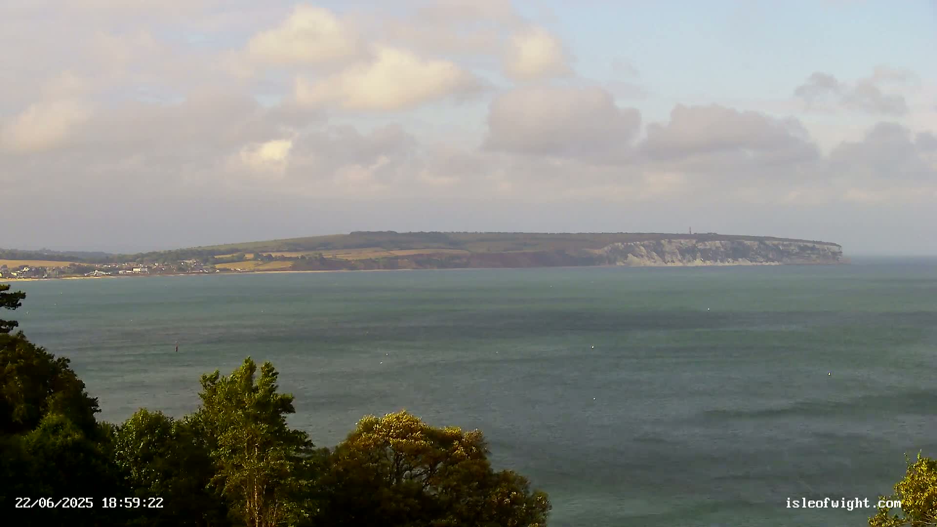 A calm body of water stretches to a distant, hilly coastline under a partly cloudy sky.