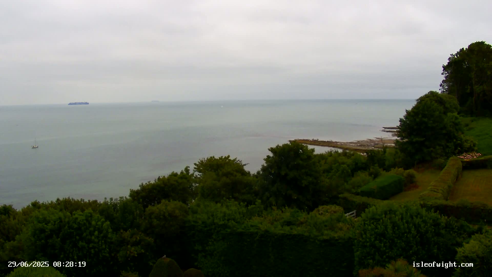 A calm, gray day overlooks a tranquil sea from a verdant hillside dotted with lush, green trees and manicured hedges.