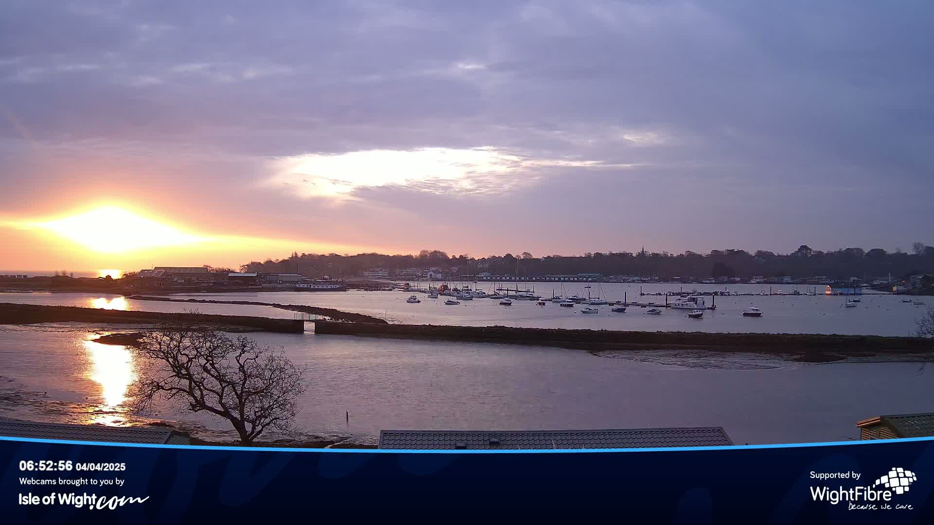 A calm harbor filled with numerous boats is viewed at sunset under a mostly clear, pastel sky.