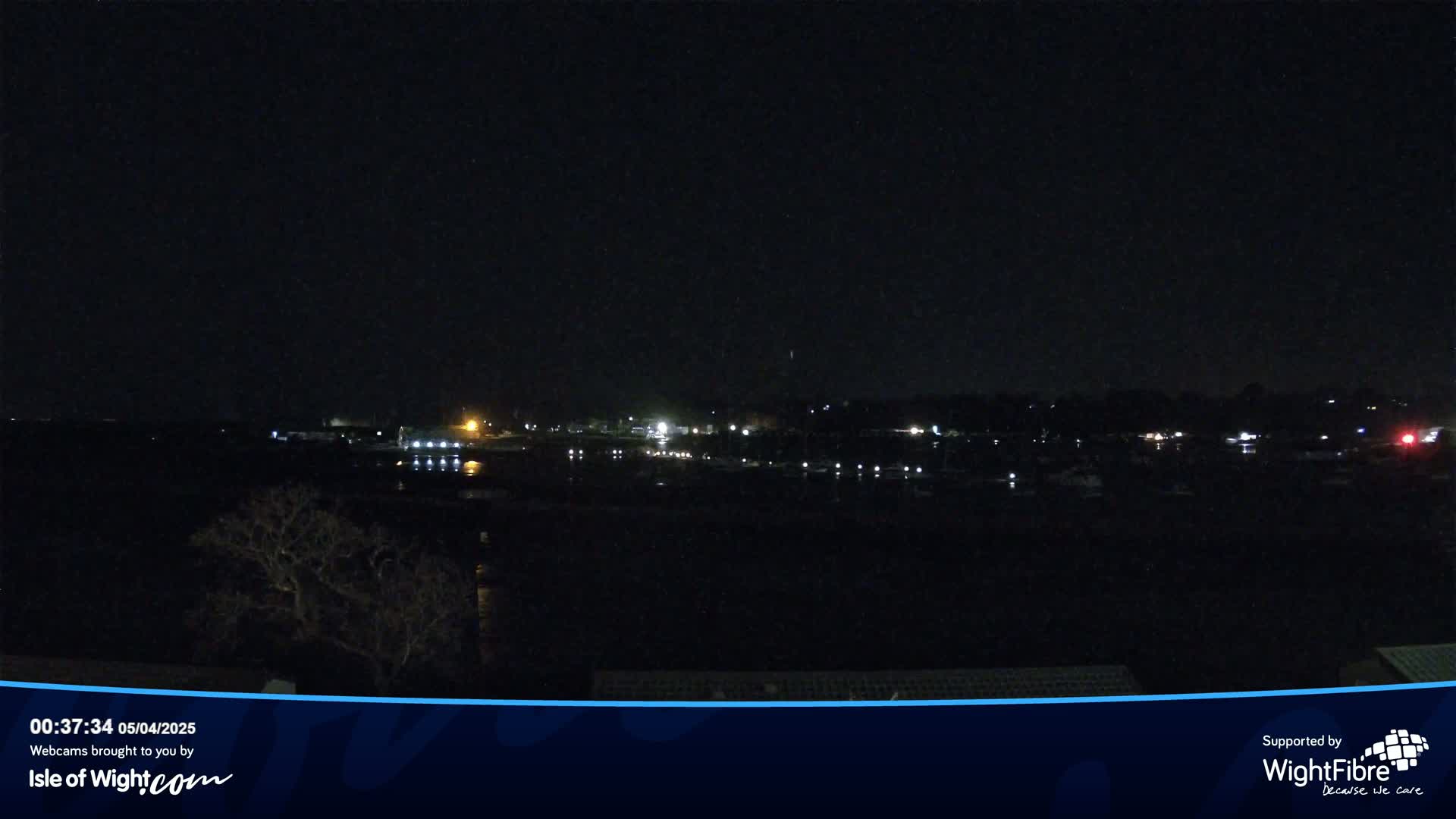 A nighttime view of a dark body of water with faintly illuminated boats and a distant shoreline with scattered lights.