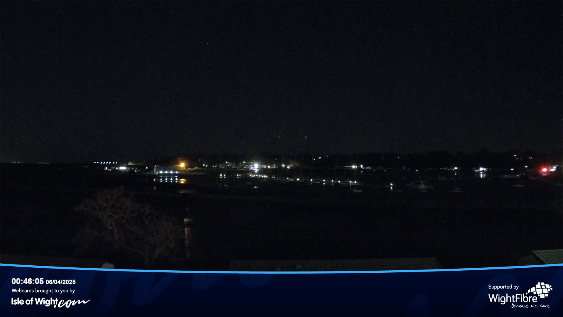 A nighttime view of a calm body of water with dimly lit boats and a shoreline with buildings.