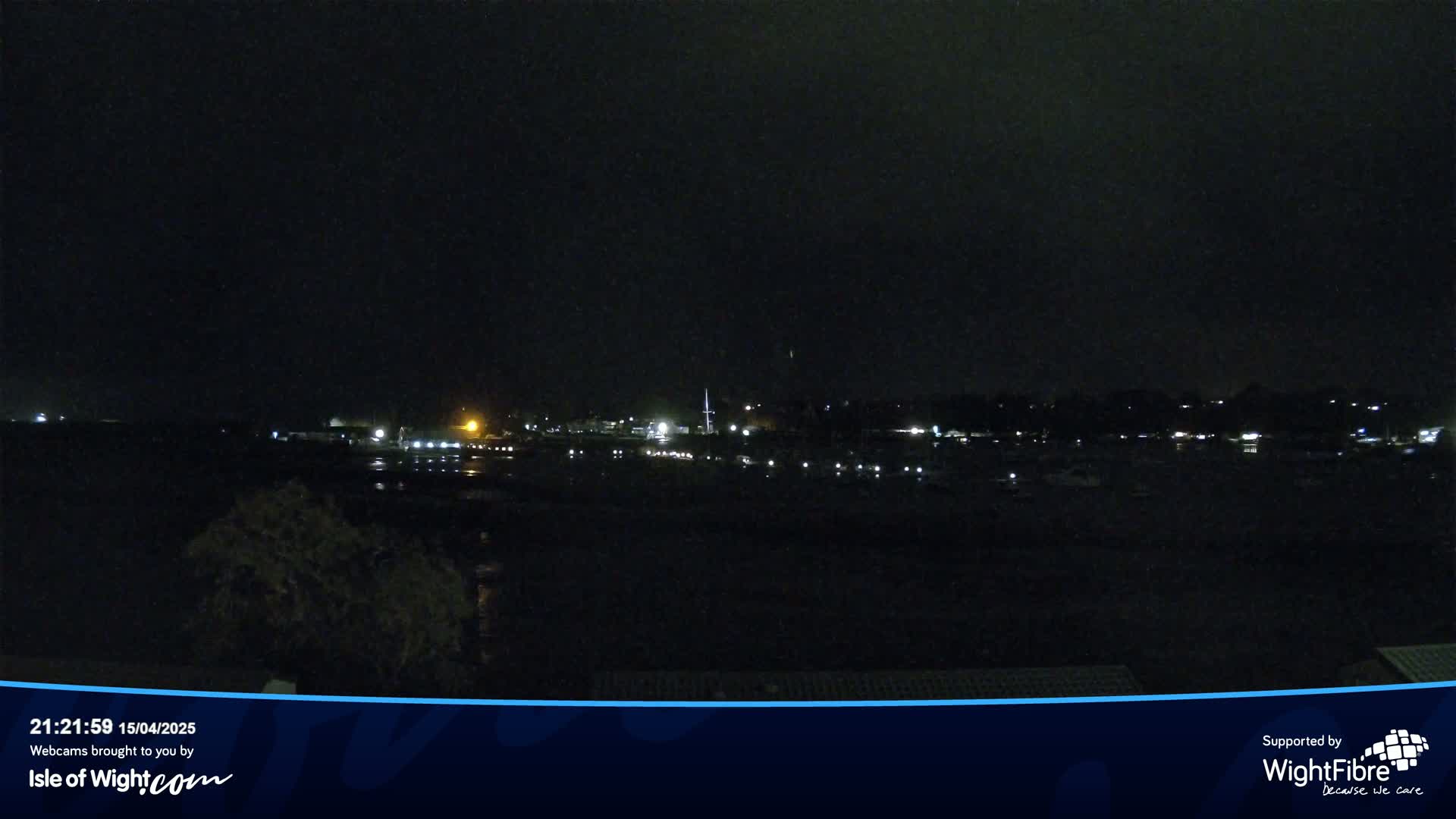 A nighttime view of a dark body of water with faintly visible lights from boats and buildings on the far shore under a dark sky.