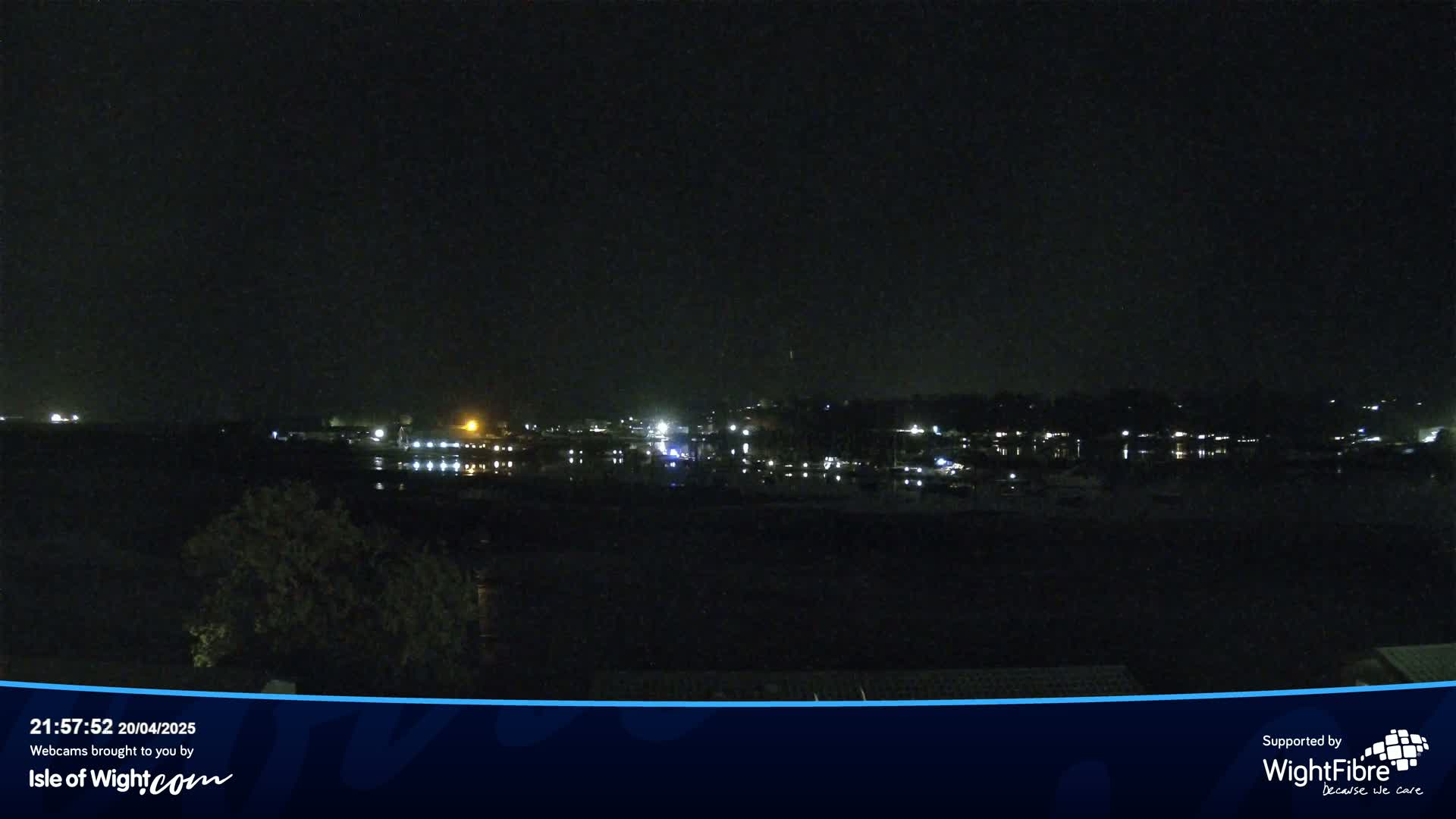 A nighttime view of a calm body of water reflecting the lights of a distant town under a dark sky.