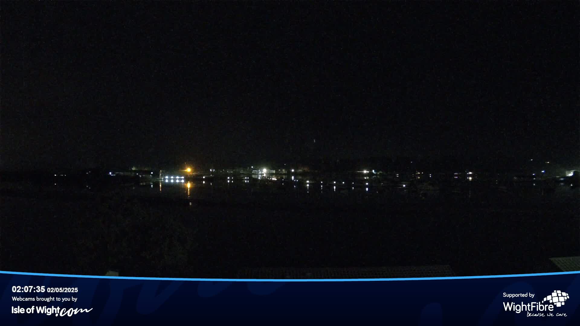 A nighttime view of a calm body of water reflecting the lights of a distant shoreline.