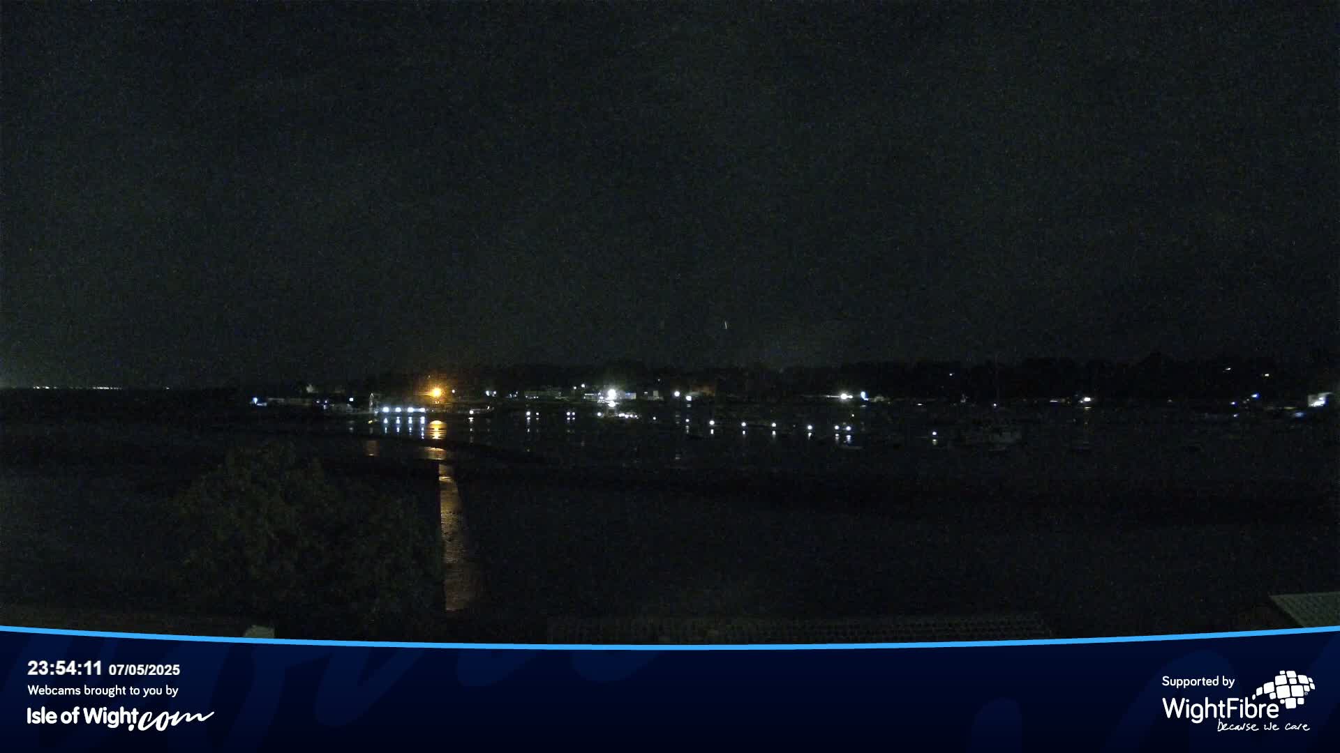 A dark nighttime view of a calm body of water reflecting the lights of a distant shoreline.