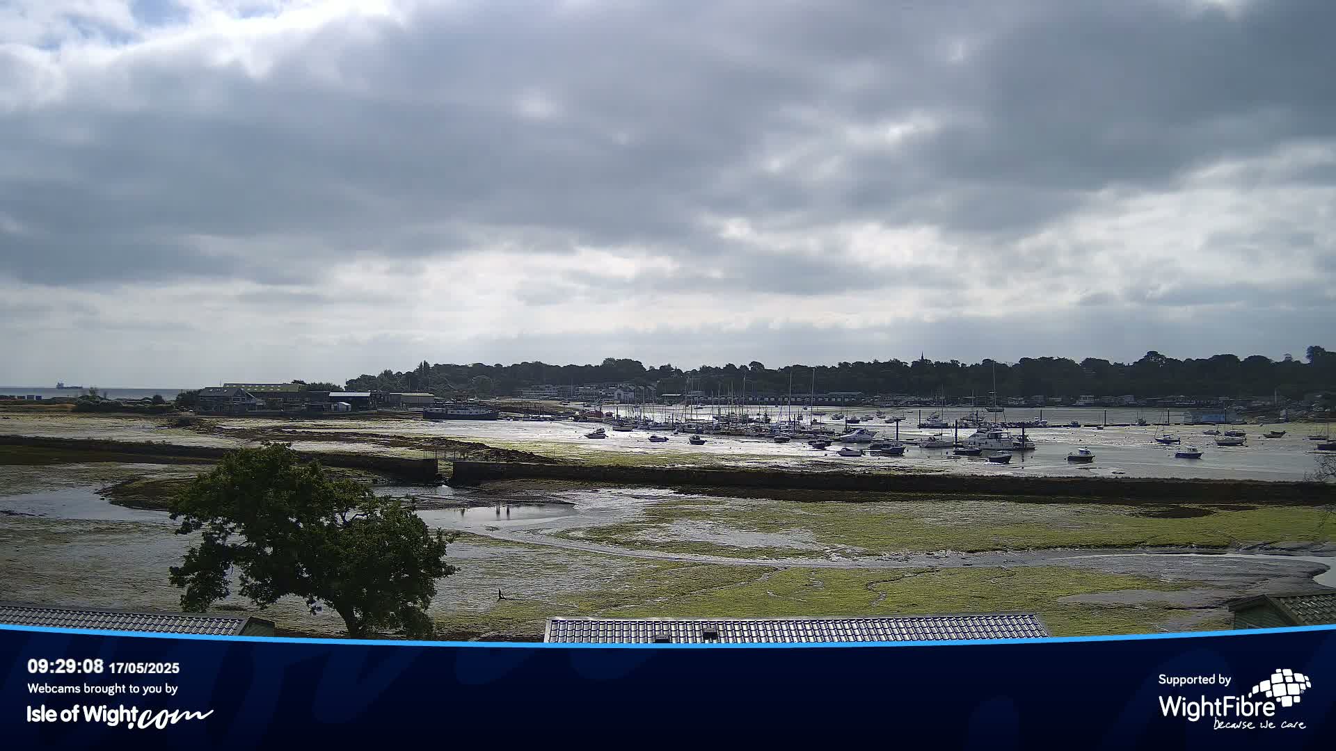 A harbor with numerous boats at low tide under a partly cloudy sky.