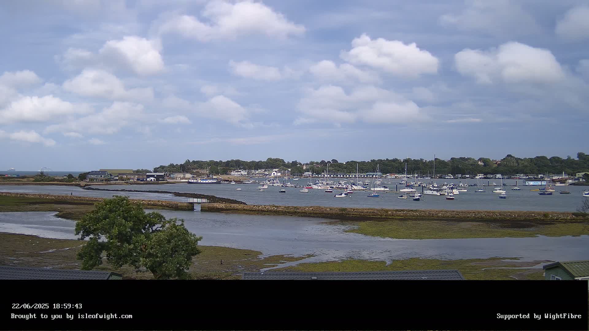 A calm bay with numerous boats and a partially cloudy sky.