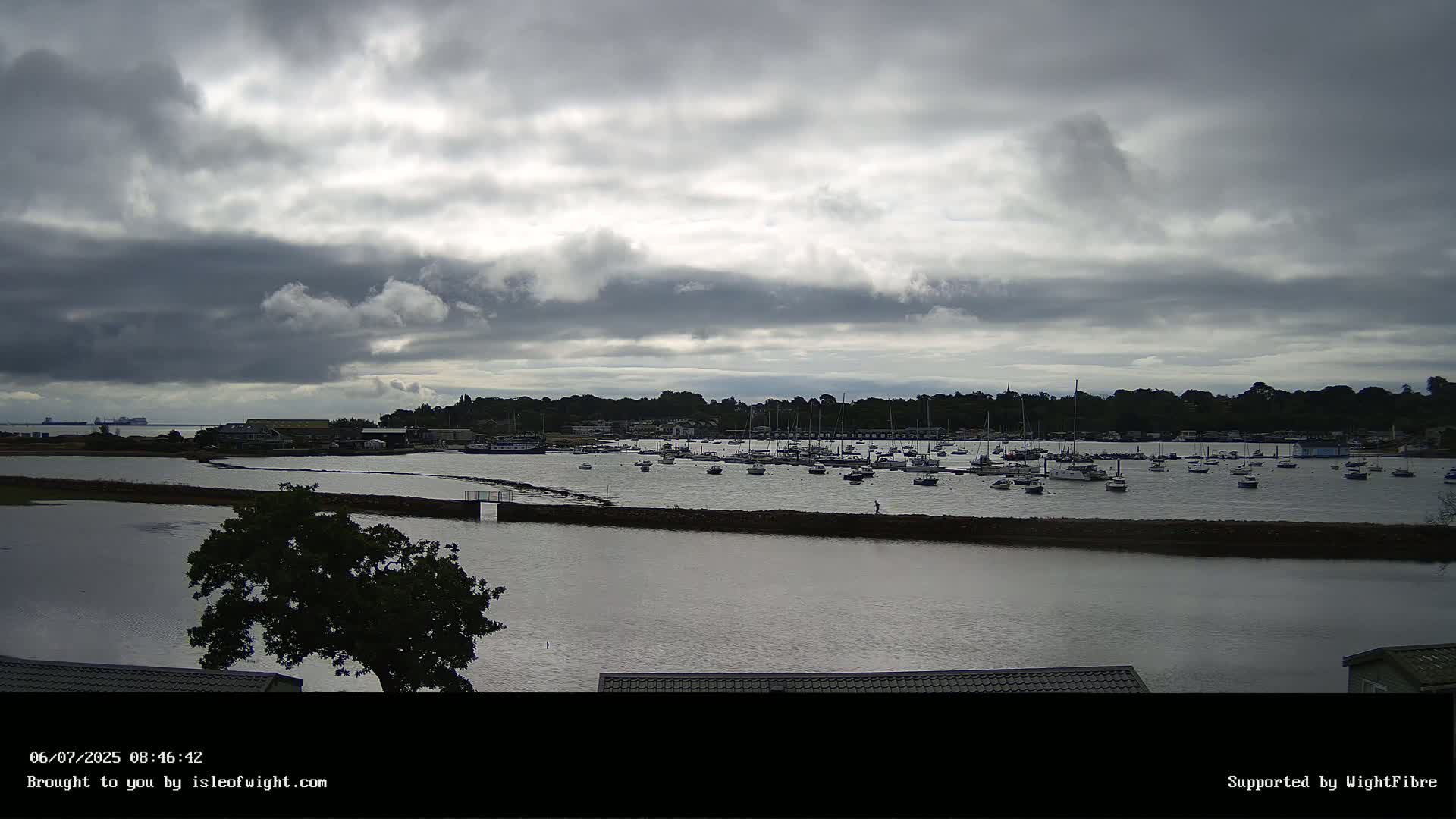 Many sailboats are moored in a calm bay under a cloudy sky.