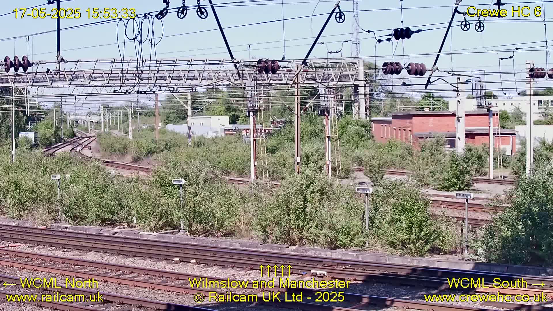 Overgrown railway tracks and electrical infrastructure are visible under a sunny sky.