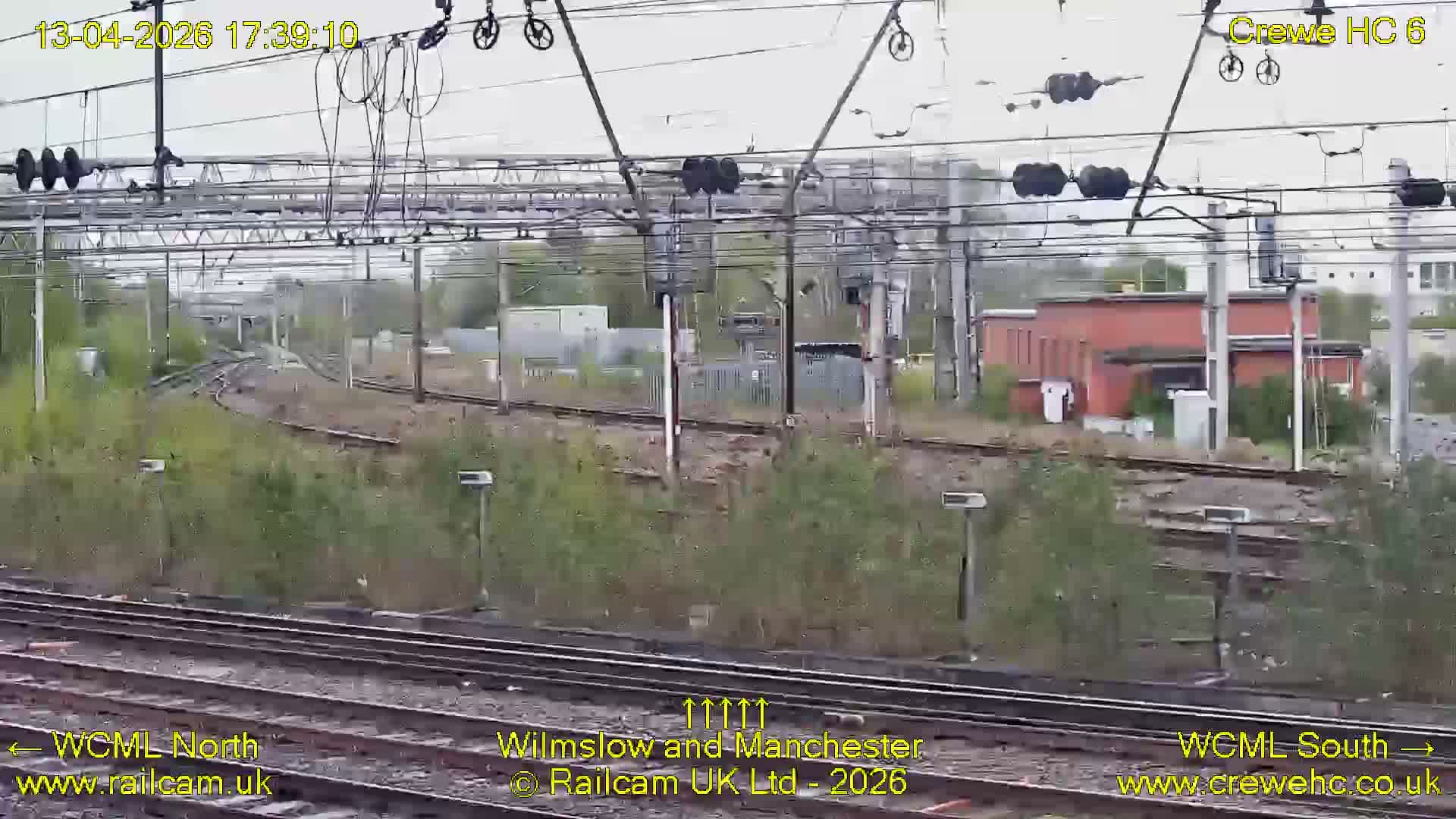 The image captures a clear early morning view of a dark railway junction featuring multiple tracks, illuminated signals, overhead power lines, and distant buildings.