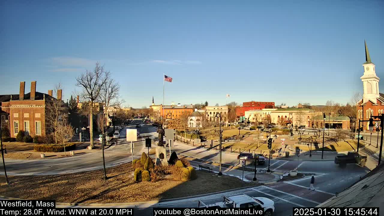 A sunny town square with brick buildings and a church steeple, under a clear blue sky with a brisk wind.