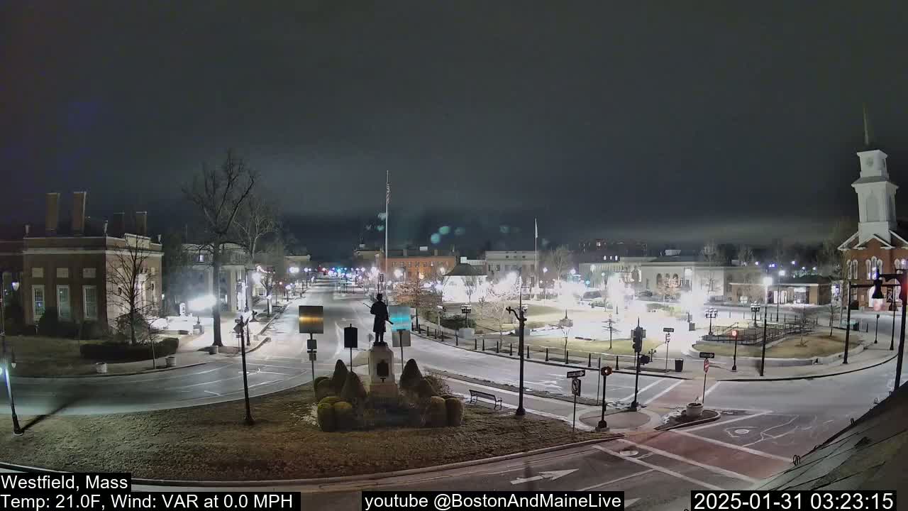 A nighttime view of a town square, with a statue in the center, under a mostly clear, dark sky.
