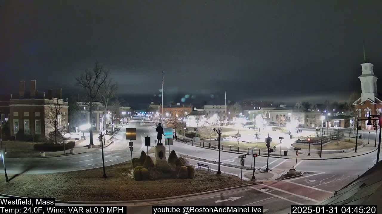 A nighttime view of a town square with a statue in the center, under a cloudy sky.