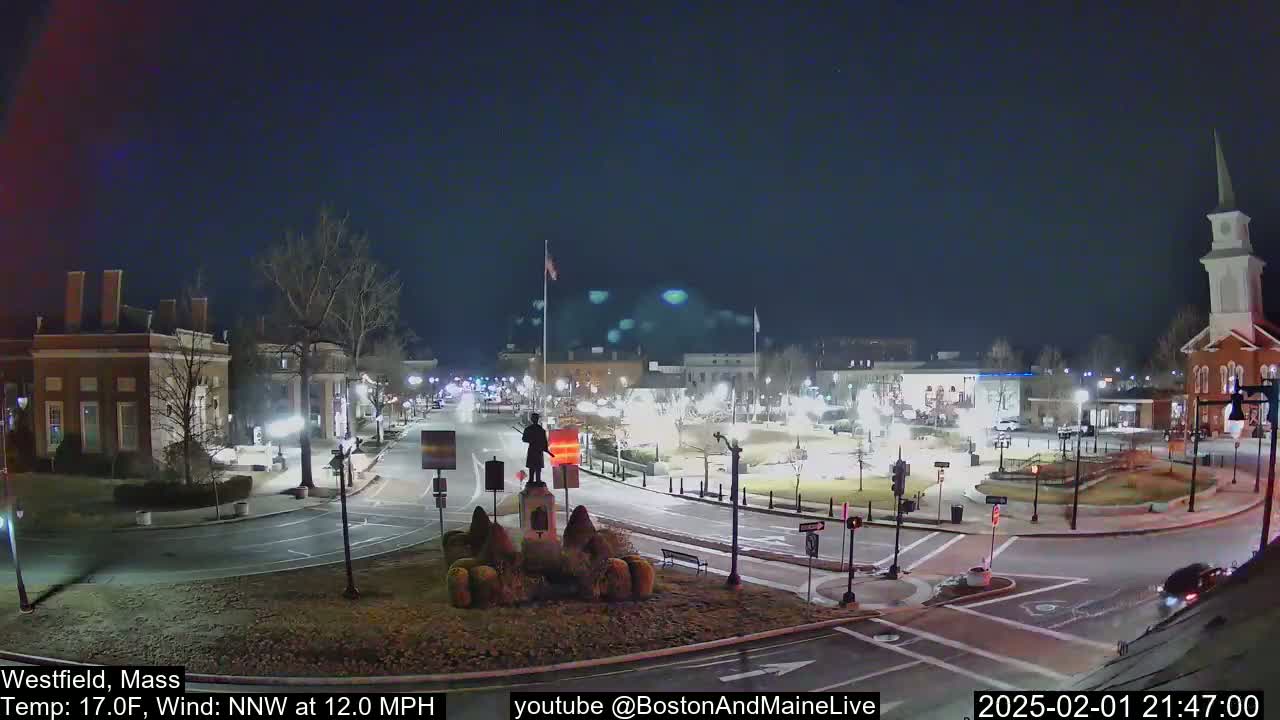 A nighttime view of a town square with a statue in the center, under a clear, cold sky with a northwest wind.