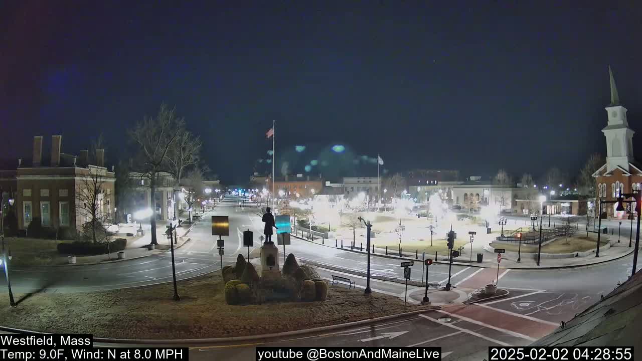 A nighttime view of a town square with a statue in the center, under a clear, dark sky, and a temperature of 9 degrees Fahrenheit.