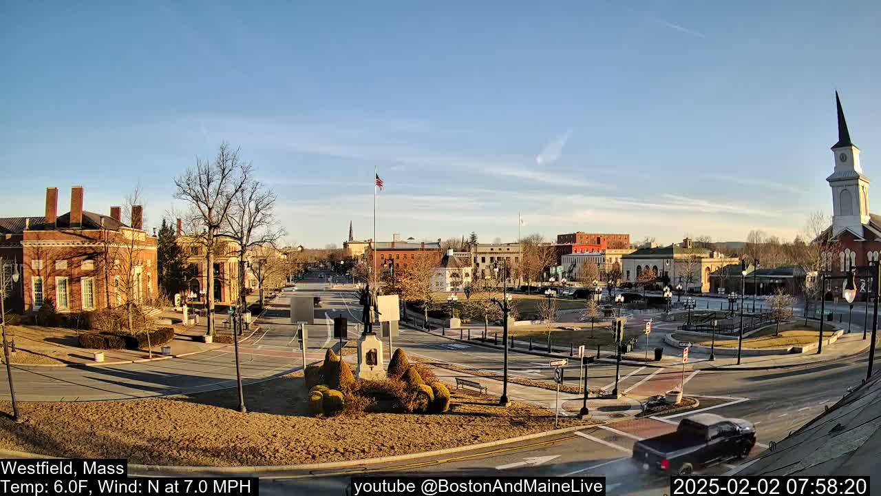 A town square with brick buildings, a statue, and a church steeple under a clear, sunny sky.