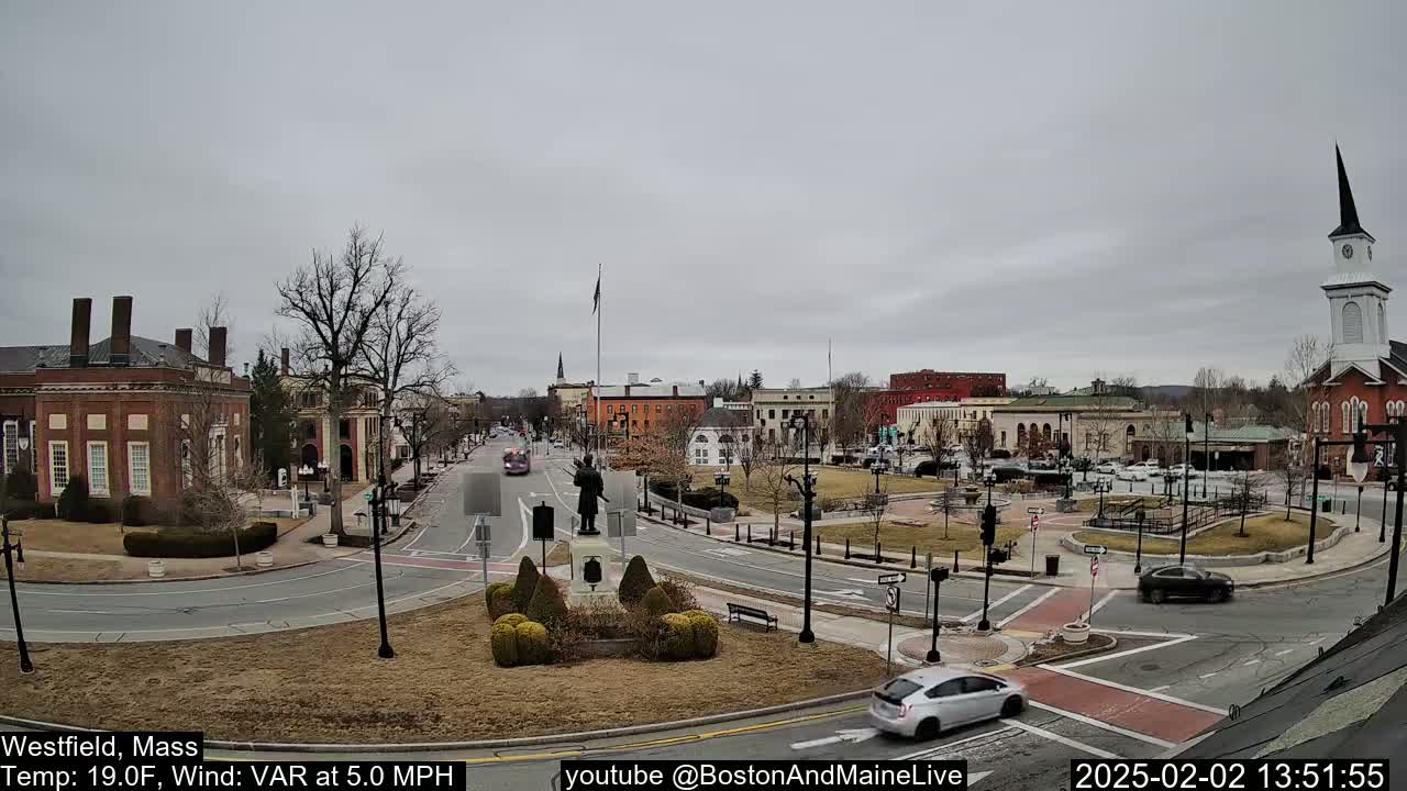 A town square with brick buildings, a statue, and sparse, bare trees under an overcast sky.